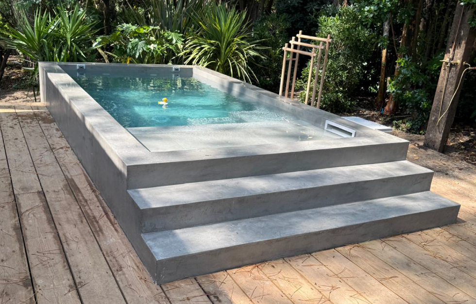 Petite piscine citadine Arcachon à fond clair avec une élégante plage immergée, bordée d'une terrasse en bois et d'un jardin verdoyant, une réalisation sur mesure par Couleur Piscine Sud Ouest.