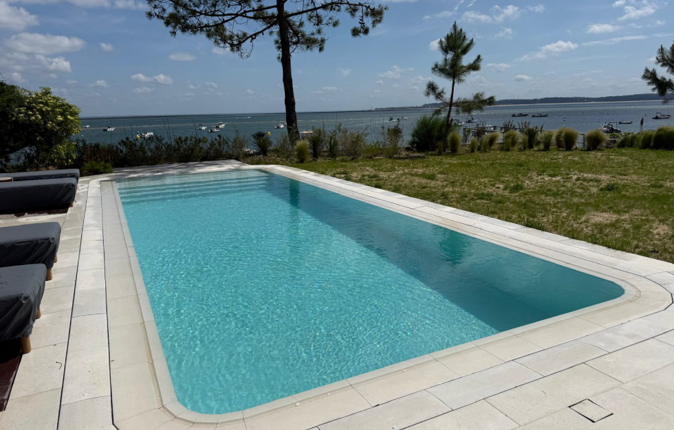 Grand bassin rectangulaire à effet miroir avec eau cristalline et large escalier immergé, surplombant le paysage maritime, conçu sur mesure par Couleur Piscine Sud Ouest, Expert piscine Lacanau.